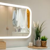 An LED mirror lights a white countertop with plants and a dispenser in soft neutral tones. A clean girl wellness vibe with subtle biophilic styling.